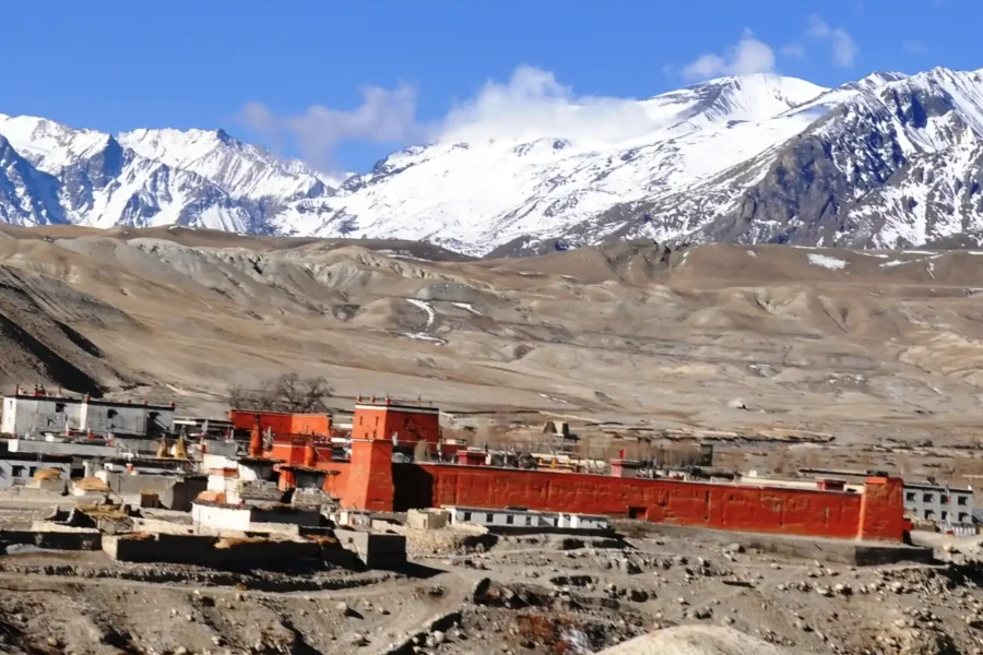 The ancient walled city of Lo Manthang in Upper Mustang, with its distinctive red palace and traditional buildings, set against a backdrop of snow-capped Himalayan mountains, a highlight of any Mustang trek.